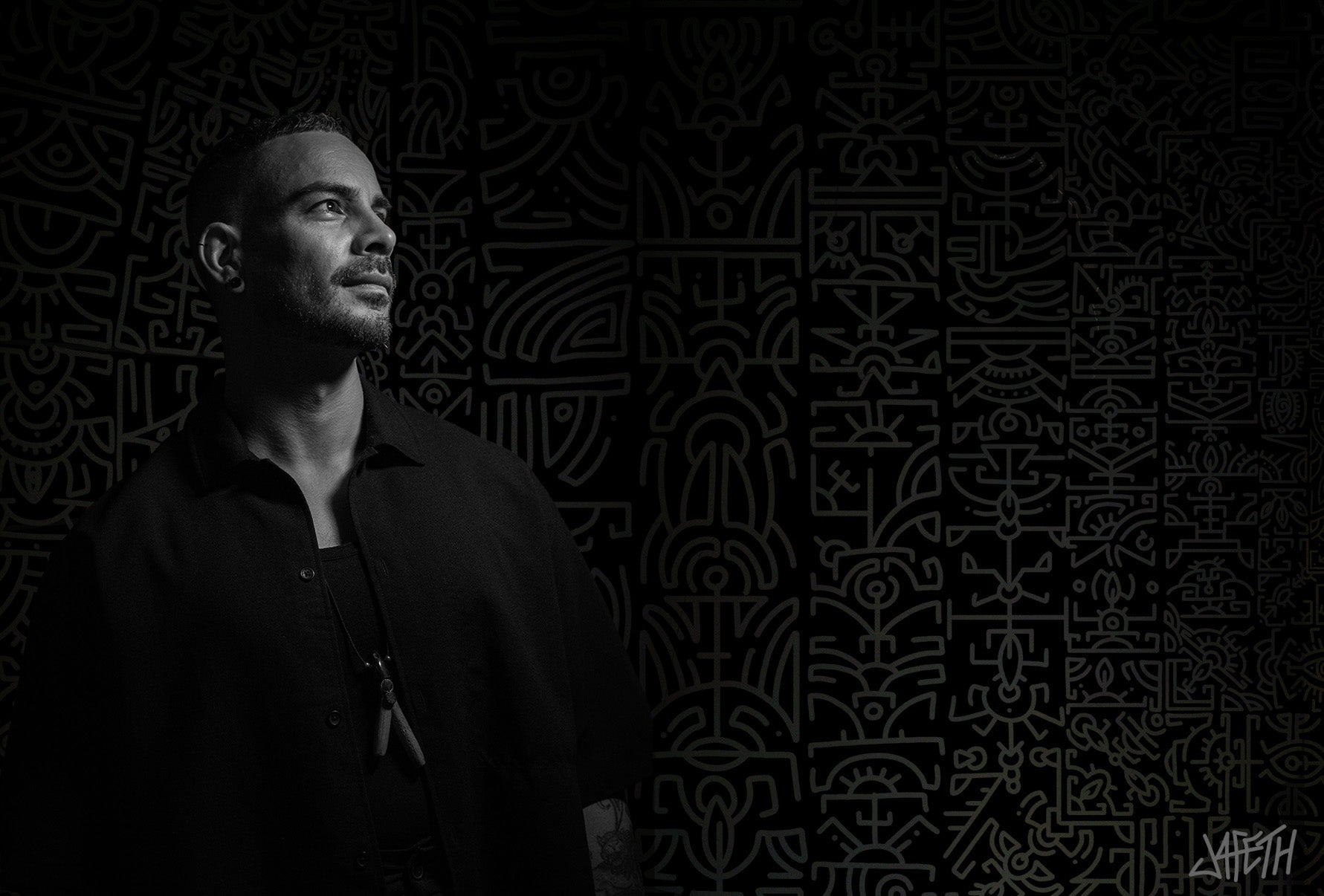 Artist Jafeth, standing against a black background with a subtle geometric pattern