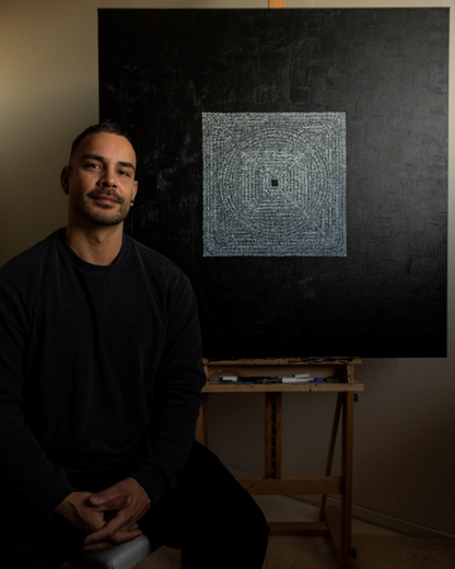 Jafeth sitting in front of a large black painting with text in a studio setting